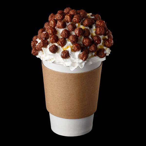 Coffee drink covered with whipped cream, chocolate syrup and candies in paper cup to go isolated on black background