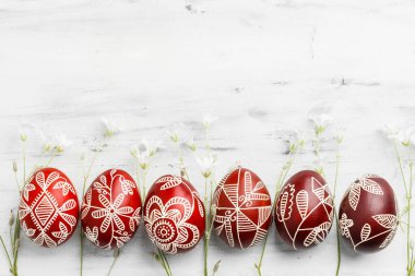 Row of red and white handmade wax dyed Easter eggs. Ukrainian pysanka frame on white wooden background with copy space for text clipart