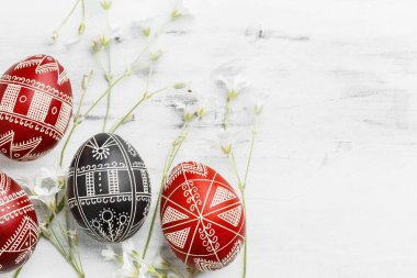 Red and black handmade Easter Pysanka eggs. Ukrainian pysanky decorated with wax-resist dyeing technique. White wooden background with copy space for text clipart