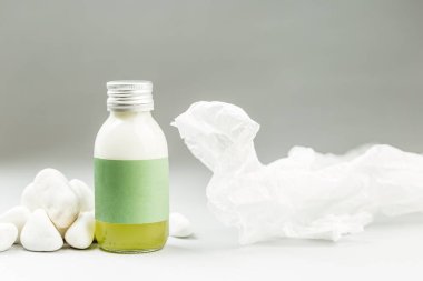 Plastiksiz Paketleme Deri Bakımı Ürünleri. Metal kapaklı cam şişe ve beyaz taşlar ve pirinç kağıt dekorasyonlu gri arka planda boş yeşil etiket