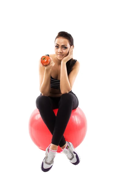 Menina está sentada na bola de fitness e segurando um tomate — Fotografia de Stock