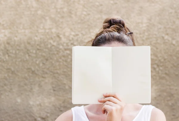 Woman hiding her face behind empty white paper notebook — Stock Photo, Image