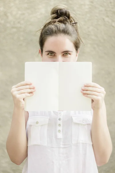 Woman hiding half of her face behind empty white paper notebook — Stock Photo, Image