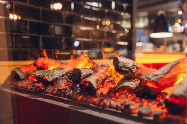 Elektrikli şömine. Restoran vitrini yapay ısıtıcıyla dekore edilmiş. Cam pencerenin arkasında yanan ahşap. Dış tasarım