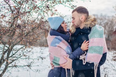 Erkek ve kadın kış ormanında yürüyor ve sarılıyorlar. İnsanlar kar altında battaniyeyle ısınıyor. Mevsimlik faaliyetler