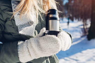Kış parkında elinde elektrikli süpürge şişesiyle çay içen bir kadın. Yürüyüş sırasında karlı ve soğuk havada ısınmak için içecekler.