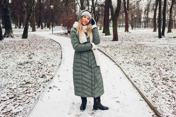 冬季时尚 在雪地的公园里 年轻的女人穿着长长的绿色外套 戴着围巾 手套和靴子 现代服装 — 图库照片