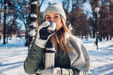 Kış parkında elinde elektrikli süpürge şişesiyle çay içen bir kadın. Yürüyüş sırasında karlı ve soğuk havada ısınmak için içecekler.