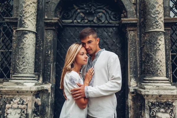 Couple in love walking in old Lviv city wearing traditional ukrainian shirts. People hug by ancient architecture landmark