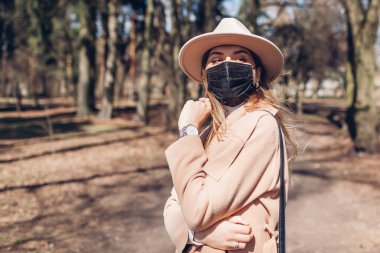 Tarz sahibi genç bir kadın, Coronavirus covid-19 salgını sırasında boş parkta yürürken açık havada tekrar kullanılabilir maske takıyor. Bahar modası