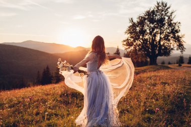 Güzel gelin, gün batımında Carpathian dağlarında mavi gelinlik içinde dans ediyor. Kadınlar çıplak sırtlı elbiseler giymekten hoşlanırlar. Arka plan