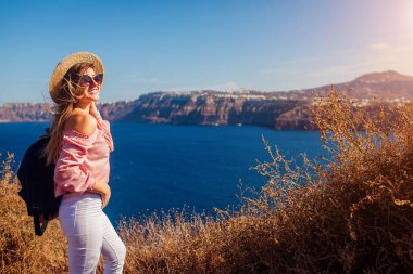 Santorini adasında yürüyen gezgin kadın, Yunanistan manzaranın tadını çıkarıyor. Sırt çantalı mutlu kız Caldera 'nın deniz manzarasının tadını çıkarıyor. Turizm