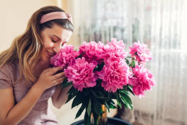 Evdeki vazoda şakayık kokusu alan bir kadın. Kız bir buket taze pembe çiçekten hoşlanıyor. Oturma odasının içini ve dekorunu.