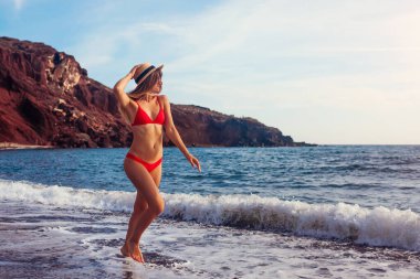 Santorini 'de Santorini' de bikinili seksi bir kadın deniz kenarında yürüyor. Mutlu kız koşuyor ve zıplıyor. Yaz tatilinin tadını çıkarıyor.