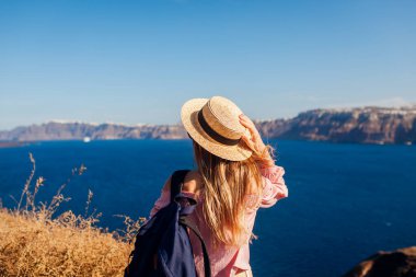 Santorini adasında yürüyen gezgin kadın, Yunanistan manzaranın tadını çıkarıyor. Sırt çantalı mutlu yürüyüşçü Caldera manzarasının tadını çıkarıyor. Turizm