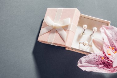 Set of pearl jewellery in pink gift box with flowers. Silver earrings and ring with lily on grey background