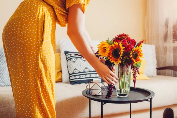 Kobieta kładzie wazon ze słonecznikami i kwiatami cynku na stole. Gospodyni domowa dba o wystrój wnętrz i jesieni w domu. — Zdjęcie stockowe