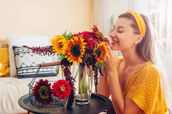 Kvinna luktar bukett solrosor med zinnia blommor arrangerar i vas hemma. Damen tycker om färska blommor. Interiör — Stockfoto