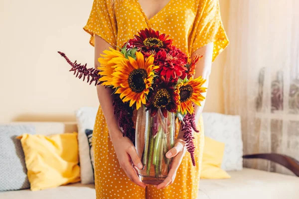 Kobieta trzyma wazon ze słonecznikami i kwiatami cynku. Bukiet jesieni czerwony żółty kwiat pomarańczy w domu. — Zdjęcie stockowe
