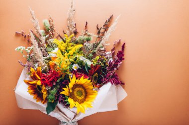 Fall bouquet of yellow red orange flowers wrapped in paper and arranged on brown background. Sunflowers, amaranth, daisies with zinnias and grasses clipart