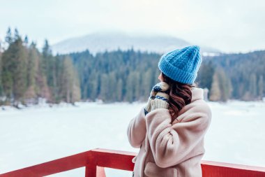 Karlı dağ gölü Synevyr manzarasına hayran olan turist beyaz kürklü bir kadın. Ukrayna 'da seyahat. Kış orman manzarası