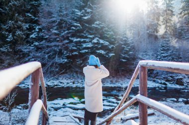 Karlı orman ve nehir manzarasına hayran olan beyaz kürklü bir kadın. Kış manzarası. Tatil için seyahat ediyorum. Dağlara yolculuk