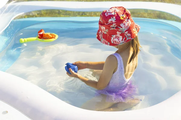 Uma menina em um chapéu de panamá vermelho joga em uma piscina, férias de verão, entretenimento de água — Fotografia de Stock
