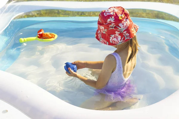 A girl in a red panama hat plays in a pool, summer vacation, water entertainment — Stockfoto