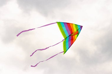 Gökyüzünde çok renkli bir uçurtma bulutların arka planında uçuyor.