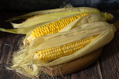 Koyu ahşap arka planda üç mısır koçanı.