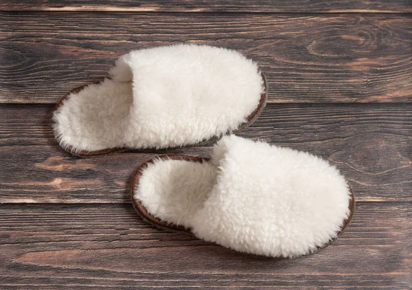 Pantuflas blancas de lana esponjosa hechas de lana de oveja sobre un fondo de madera —  Fotos de Stock