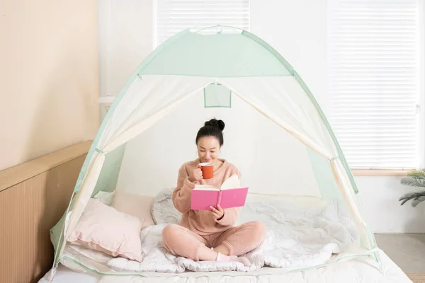 Asian woman in pajams under indoor bed tent