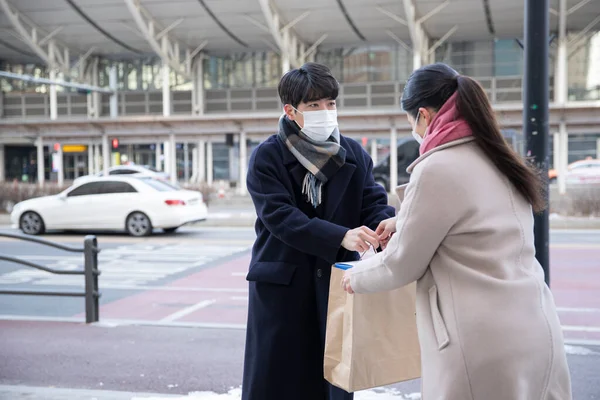 Asian woman and man with face masks handing over paper bag, face to face selling second hand stuffs concept