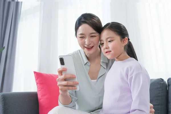 アジアの母親と若い娘はスマートフォンを使いながら笑顔で — ストック写真