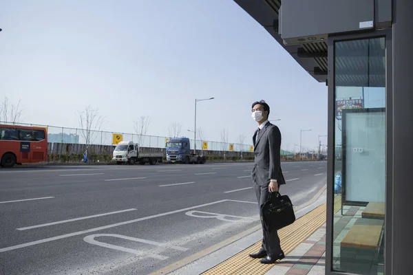 バスの駅でマスクを身に着けているスマートカジュアルなスーツのアジア人男性 仕事への道 — ストック写真