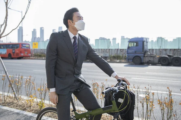 Asian man in smart casual suit wearing mask on bicycle, on the way to work