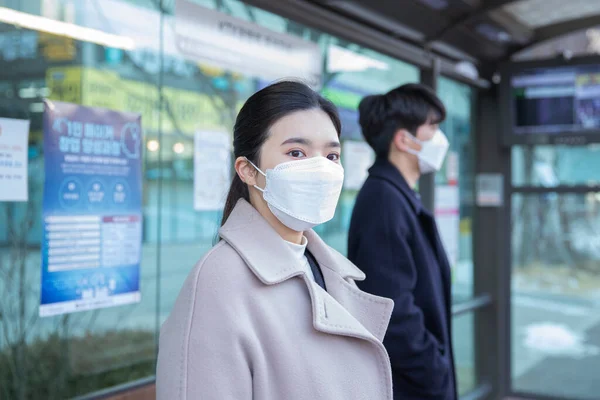 Asian man and woman with mask at bus station, wearing mask in public transportation
