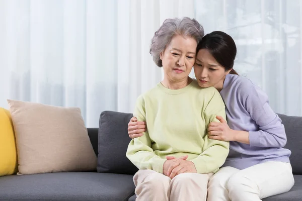 depressed Asian old mother comforted by middle aged daughter