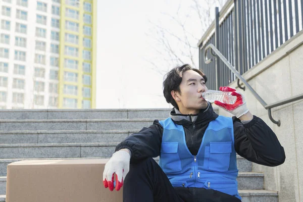 Asian delivery man drinking water in stairs