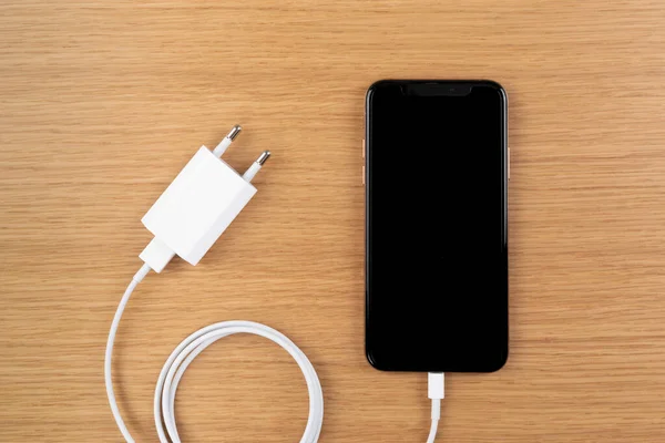 Smartphone and charger adapter placed over wooden background