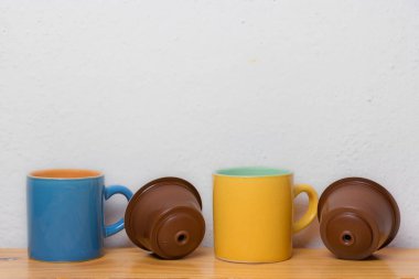 mavi ve sarı fincanlar ve ahşap tabanlı kahve kapsülleri ve...