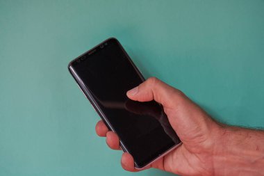 Sağ el yeşil arka planda bir cep telefonu tutuyor.