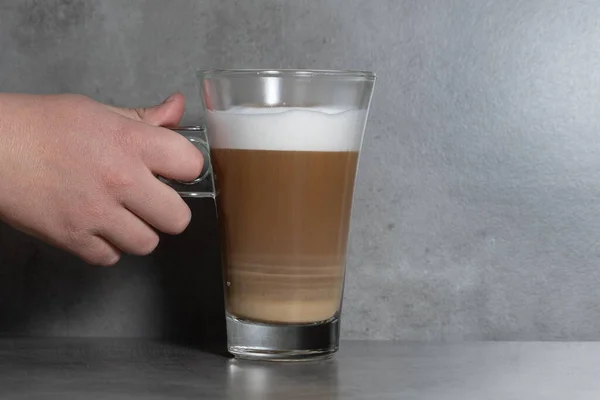 Ręczne Trzymanie Przezroczystej Filiżanki Kawy Mlekiem Pianką Szarym Tle — Zdjęcie stockowe