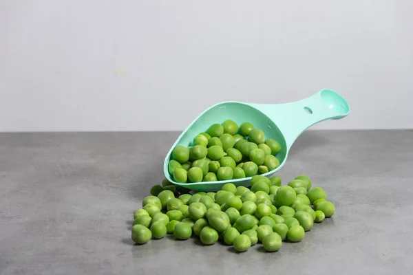 Aqua green plastic measuring spoon with serving of fresh raw peas on gray base with white background