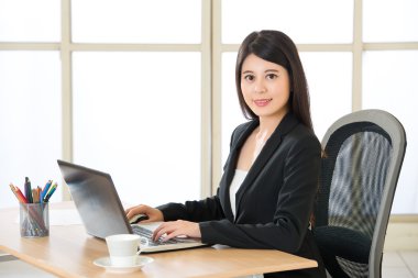 Dizüstü bilgisayar ve içecek kahve masasında kullanarak Asya girişimci gülümseyen