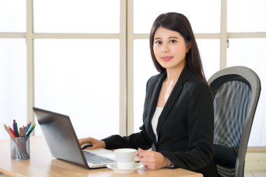 Dizüstü bilgisayar ve içecek kahve masasında kullanarak Asya girişimci gülümseyen