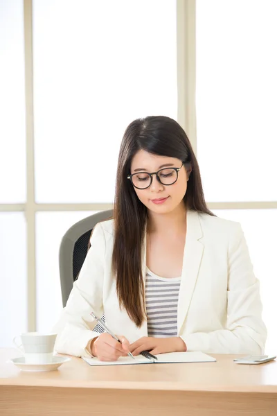 Junge asiatische Geschäftsfrau lächelt und schreibt am Schreibtisch — Stockfoto