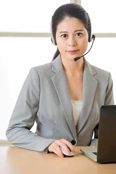 Sonriendo mujer asiática con un auricular y trabajando en el ordenador portátil — Foto de Stock