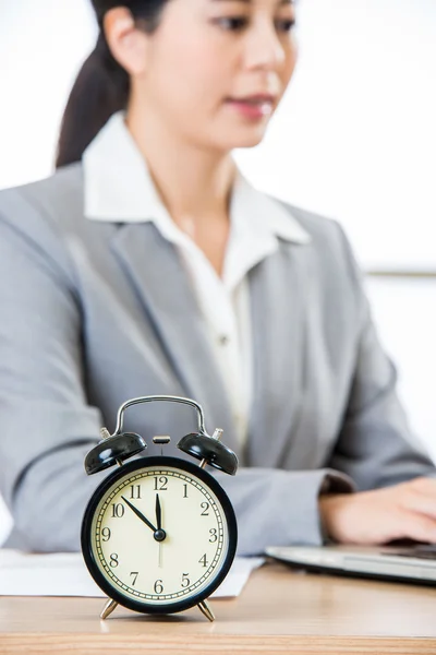 Geschäftsfrau arbeitet an Laptop mit Uhr, die Zeit anzeigt — Stockfoto