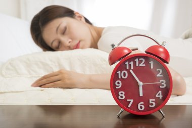 Woman sleeping in bed beside alarm clock clipart